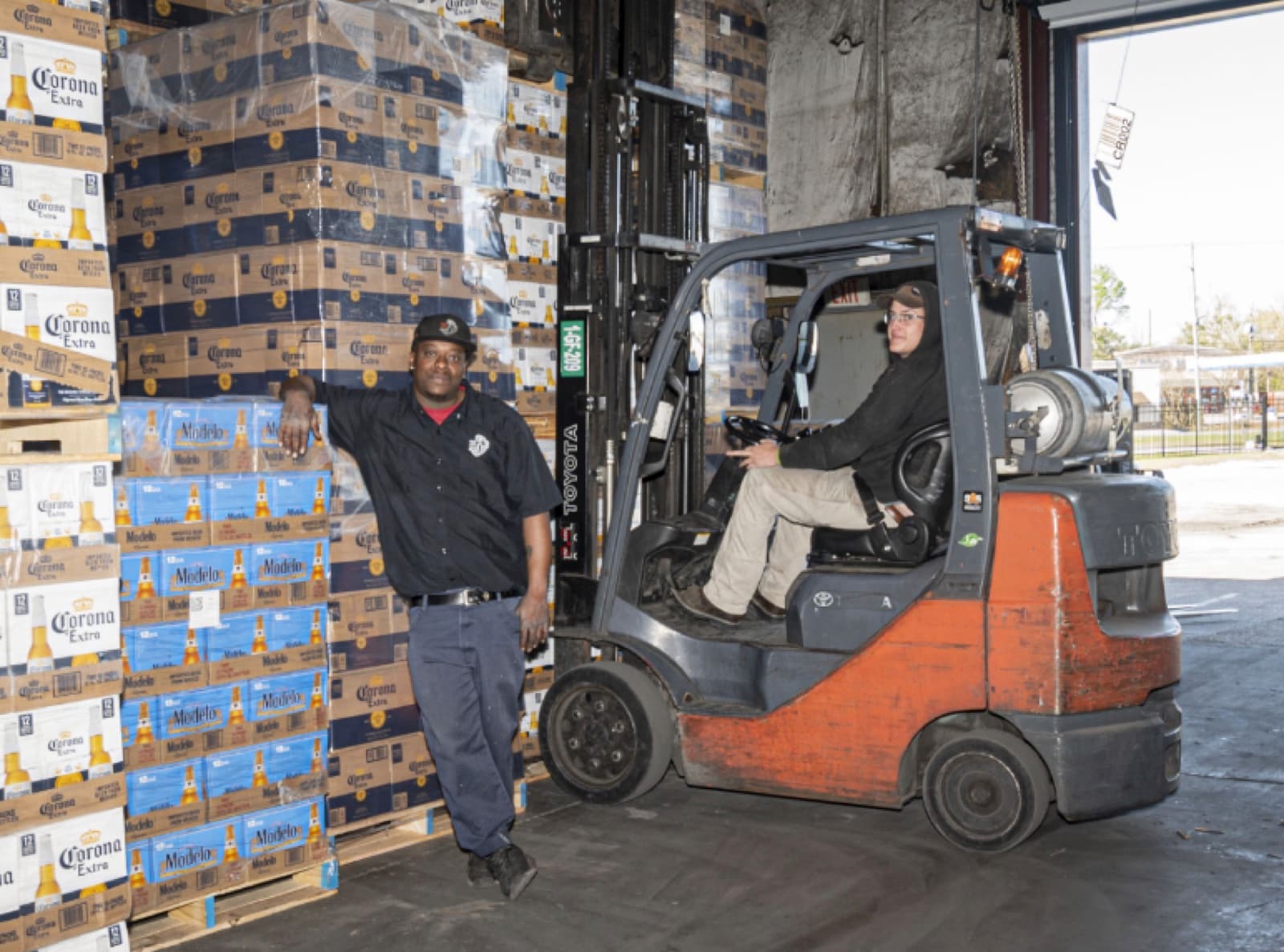 Distributor warehouse: operators with a forklift and pallets of beverage cases.